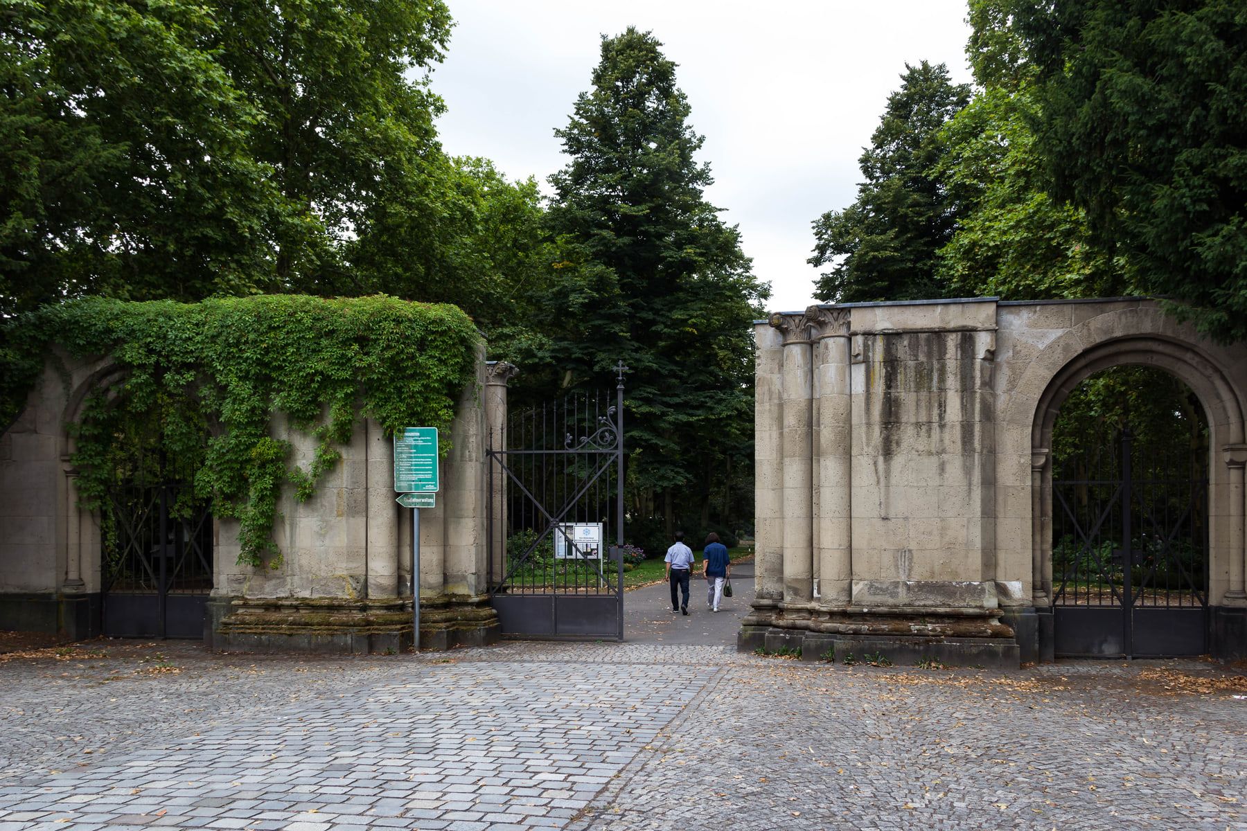 Monumentale steinerne Toranlage an der Kölnstraße mit geöffnetem schmiedeeisernem Haupttor, Rundbogenpforten und Efeubewuchs auf Nordfriedhof Bonn