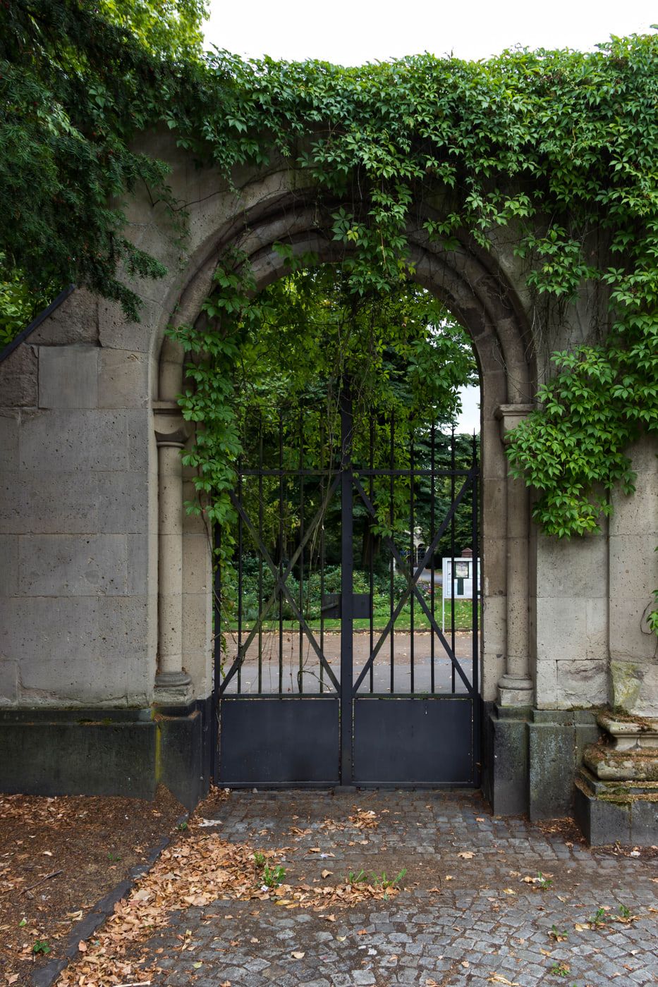 Nahansicht einer efeuumrankten steinernen Rundbogenpforte mit geschlossenem schwarzem Gittertor auf Nordfriedhof Bonn