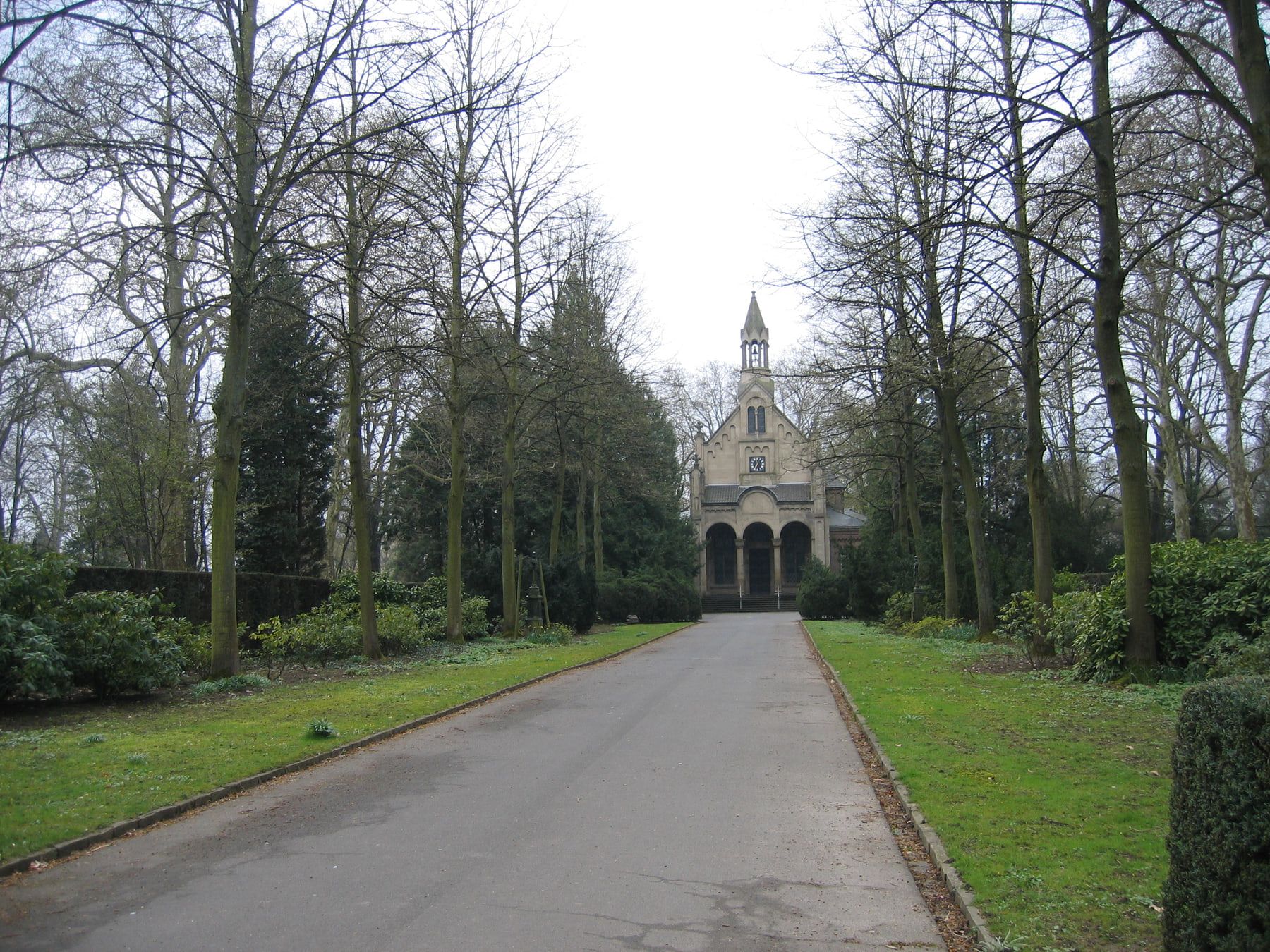 Eine symmetrische, von hohen laublosen Bäumen gesäumte Hauptallee führt direkt auf die Kapelle des Bonner Nordfriedhofs zu. auf Nordfriedhof Bonn