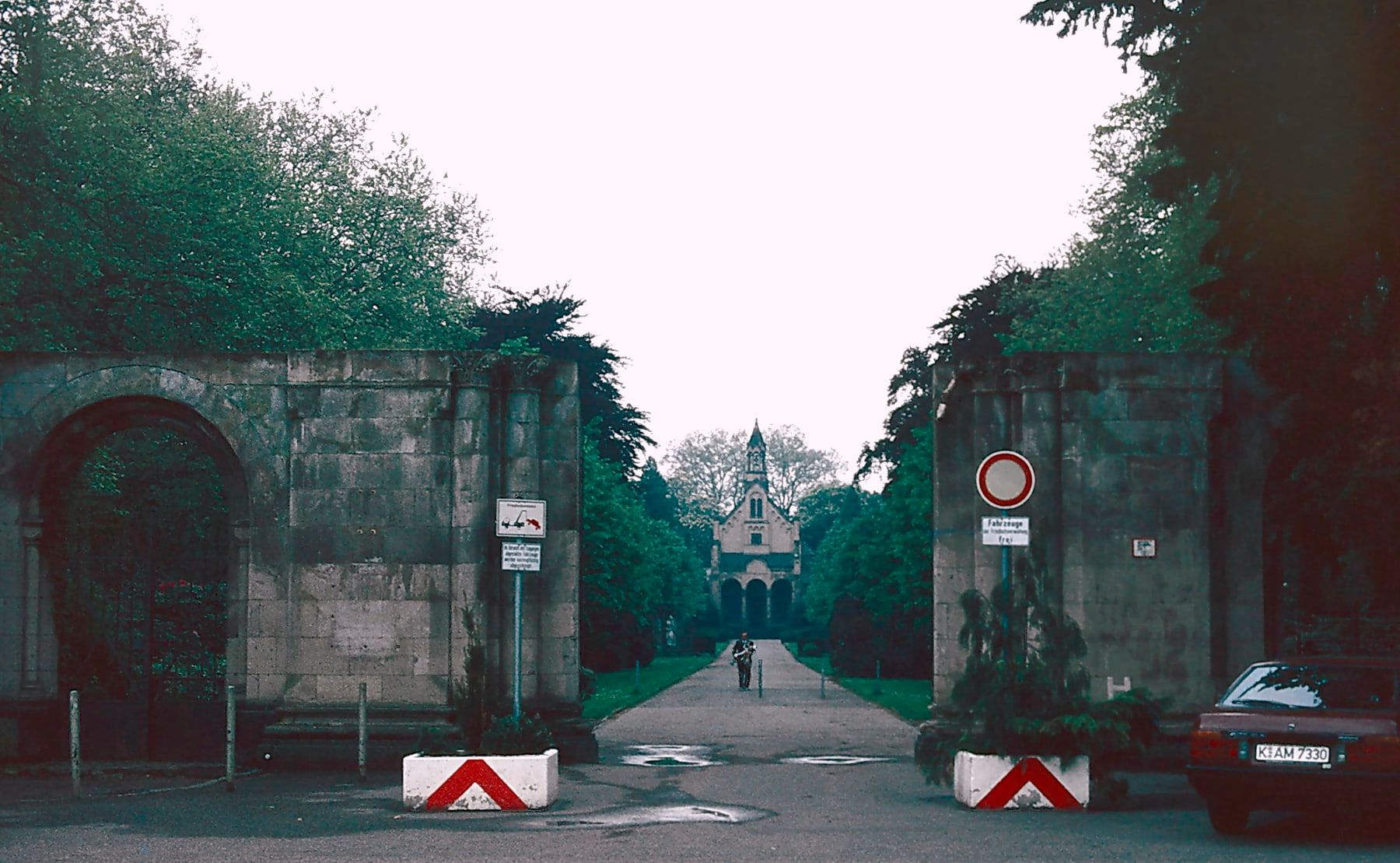 Die steinernen Reste des monumentalen Eingangs an der Kölnstraße rahmen die lange Sichtachse durch den Friedhof bis zur Kapelle. auf Nordfriedhof Bonn